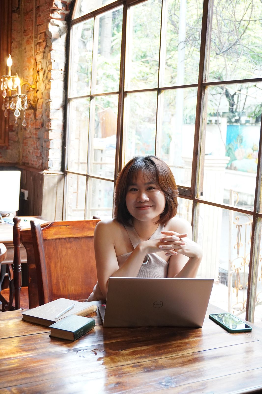 Hoa ngồi bên bàn gỗ cạnh cửa kính lớn
