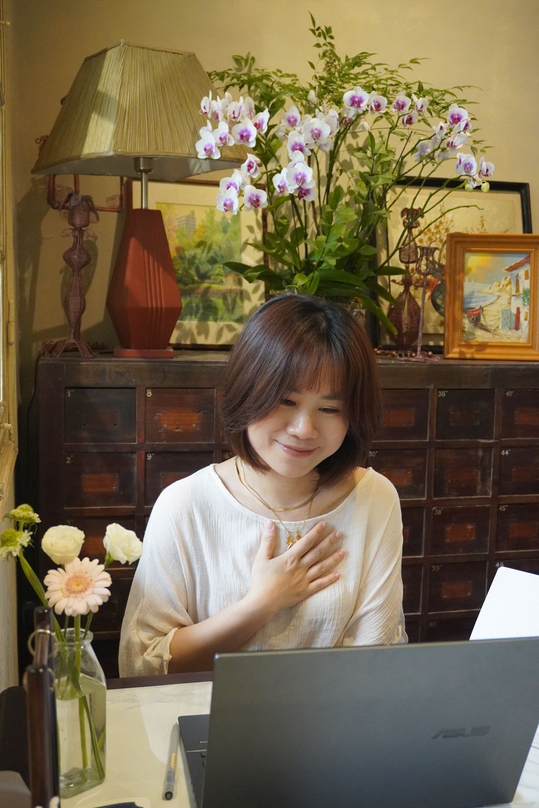 Hoa ngồi bên bàn làm việc, tay đặt lên ngực