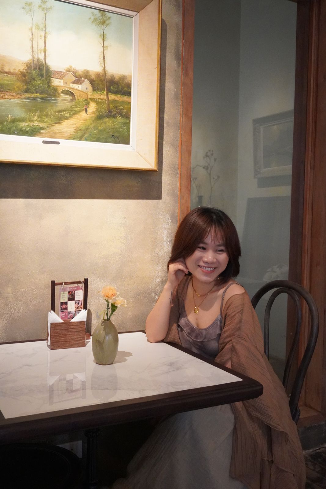 Hoa ngồi bên bàn cạnh cửa sổ, ánh sáng dịu